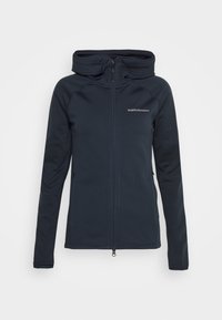 Veste noire zippée avec col montant et manches longues, comprenant deux poches latérales et un petit logo blanc "Peak Performance" sur la poitrine gauche.