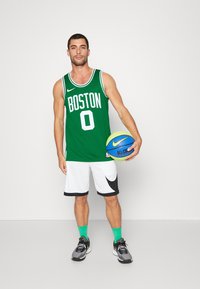 Zelena košarkaška majica s natpisom "BOSTON" i brojem "0", bijele kratke hlače s crnim akcentima, crne tenisice i drži šarenu košarkašku loptu.