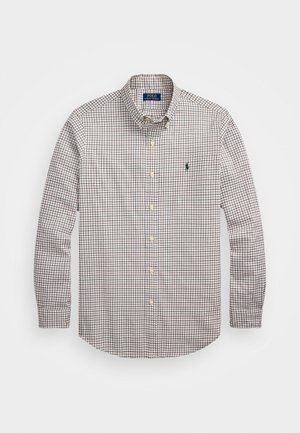 Chemise à manches longues boutonnée avec un motif à carreaux beige, marron et noir et un petit logo vert sur la poitrine gauche.