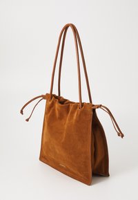 Brun semsketotebag med lange lærhåndtak og snor på sidene, myk tekstur og minimalistisk design.