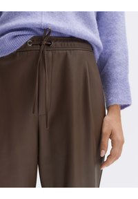 Bruine neplederen broek met een trekkoord in de taille, gecombineerd met een lichtpaarse gebreide trui, die een zachte textuur en een gladde afwerking laat zien.