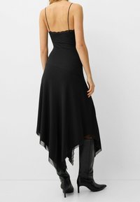 Czarna sukienka z koronkowym wykończeniem i regulowanymi ramiączkami, z asymetrycznym dołem i zwiewną tkaniną, która elegancko układa się na sylwetce. Połączona z botkami sięgającymi do kolan.