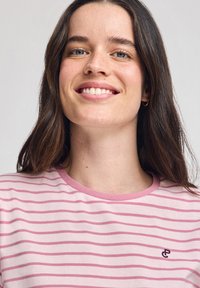 Camisa de manga corta a rayas en rosa claro y blanco, con una textura suave y un cuello rosa contrastante. Presenta un pequeño logo bordado.