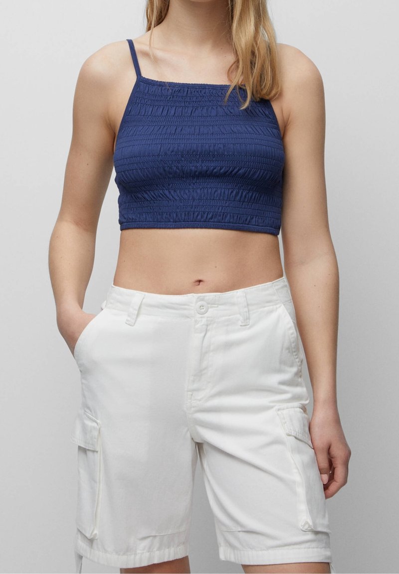 Marineblå crop top med struktureret stof og tynde stropper, parret med hvide cargo shorts med sidelommer og en afslappet pasform.