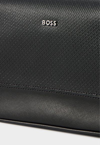Gros plan sur un sac en cuir noir texturé, orné d’un petit logo BOSS argenté et d’un panneau inférieur surpiqué.
