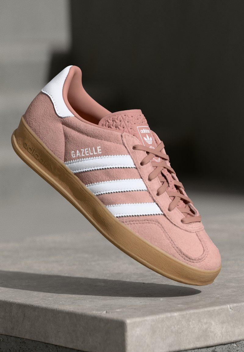 Roze suede tenisice s bijelim prugama, gumeni potplat, teksturirani gornji dio i logo na jeziku. Klasičan niskoprofilni dizajn.