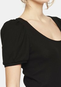 Czarny prą żkowany top z krótkimi bufiastymi rękawami i szerokim dekoltem w kształcie łódki. Materiał wydaje się elastyczny o gładkiej fakturze.