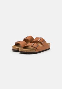 Brown faux-leather sandals with two adjustable buckles, cork footbed, and textured brown rubber sole, featuring a minimalist design.