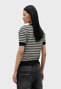 Prugasta pletena majica u crnoj i krem boji s kratkim rukavima i čvrstim crnim obrubom, s akcentima od zlatnog hardvera na ramenima. Nosena uz tamne traperice.