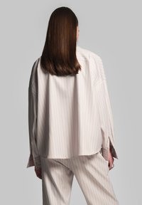 Lichtroze, losvallend gestreept shirt met verlengde schouders, zijslitsen en een zachte textuur, gecombineerd met bijpassende broek.