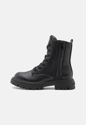 Bota de combate negra de cuero hasta media caña con cordones, cremallera lateral y suela gruesa y resistente, con la marca "Calvin Klein Jeans" en el panel de la cremallera.