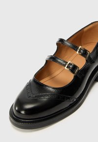 Schwarze Lederschuhe mit zwei Schnallenriemen, abgerundeter Spitze, Brogue-Details und einer strukturierten Oberfläche. Fester Absatz und glattes Innere.