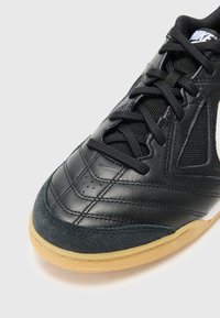 Schwarzer Leder-Laufschuh mit strukturierten Oberflächen, Mesh-Einsätzen, schwarzen Schnürsenkeln und einer Sohle aus Gummi. Mit weißem Logo und genähten Akzenten.