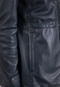 Close-up of a dark blue leather jacket sleeve and side pocket with visible stitching and a snap button cuff detail.