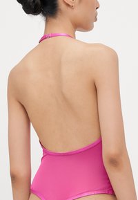 Maillot de bain rose à col halter avec un dos plongeant, fabriqué à partir d'un tissu lisse. Il dispose d'une fermeture au cou et de détails de couture minimalistes.