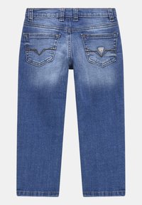 Jeans in denim blu con due tasche posteriori, una delle quali presenta una piccola toppa triangolare con il logo del marchio Guess.