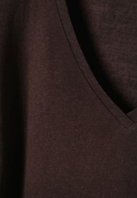 Gros plan sur un tissu marron foncé montrant une texture douce et lisse avec une couture en forme de V au niveau de l'encolure.