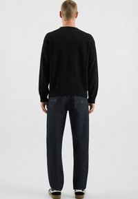 Pull en tricot noir avec un col rond, associé à un jean en denim bleu foncé. Les jeans présentent des poches arrière classiques avec des coutures jaunes.