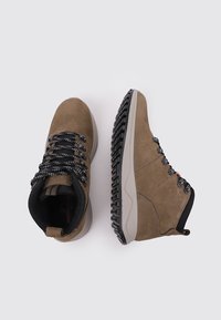 Botas de senderismo marrones con cordones negros y blancos, ojales de metal y suelas negras texturizadas, mostradas desde vistas superior y lateral sobre un fondo blanco.