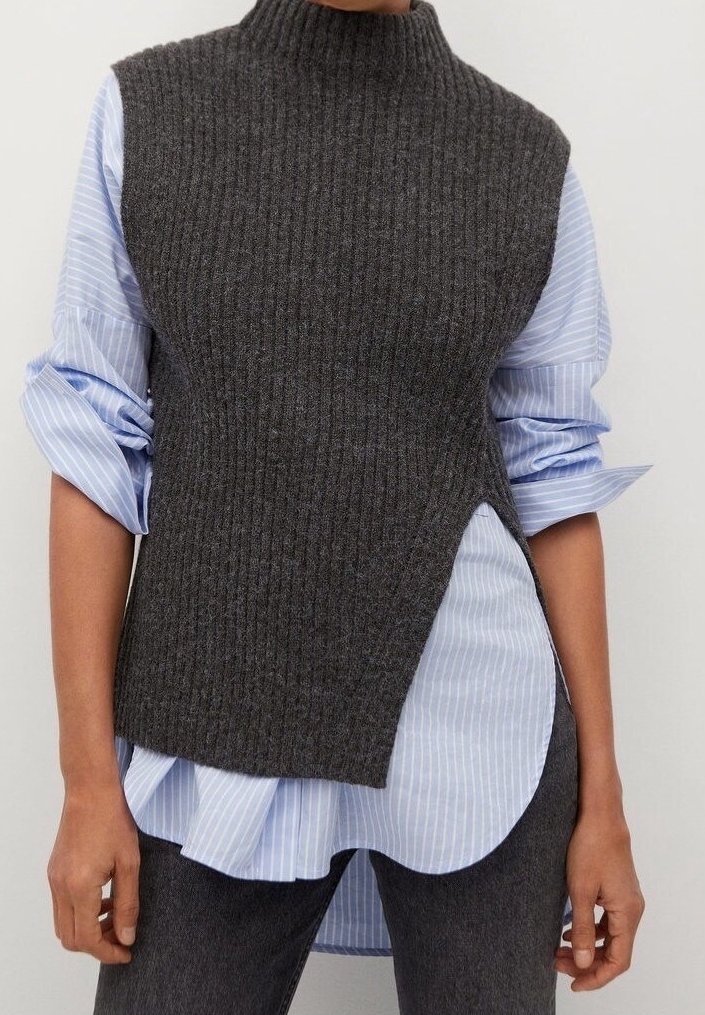 Gilet sans manches en maille côtelée gris foncé porté sur une chemise à rayures bleu clair et blanc avec manches retroussées.