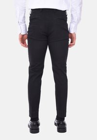 Pantaloni neri, slim-fit, con una texture liscia, dotati di tasche posteriori e orli arrotolati, abbinati a scarpe nere.