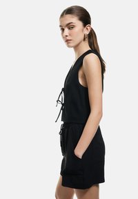 Zwarte mouwloze jumpsuit met een v-hals en verstelbare strik aan de voorkant, voorzien van een elastische tailleband, zijzakken en een ontspannen pasvorm.