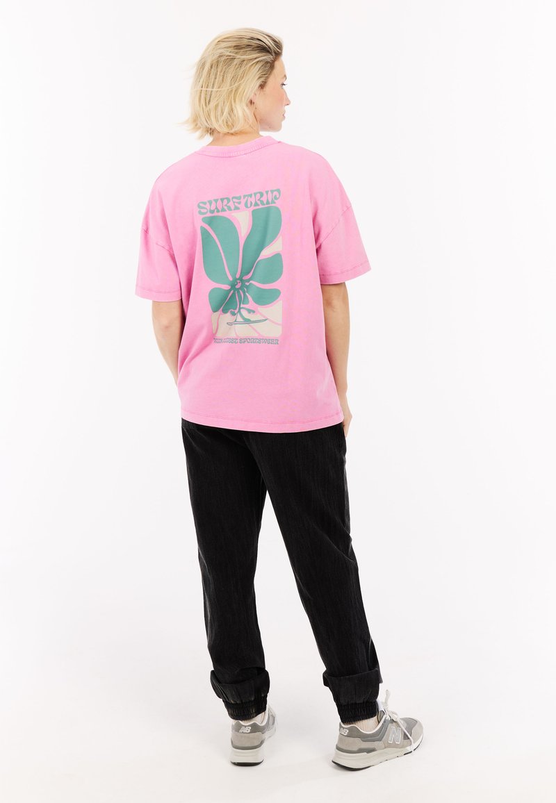 Roze oversized t-shirt met een groene bloemenprint op de achterkant. Gecombineerd met donkere broek en grijze sneakers.