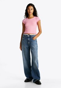 Różowa prążkowana krótka koszulka z falbaniastymi krawędziami, zestawiona z luźnymi niebieskimi d�żinsami z subtelnymi detalami. Czarnych butów dopełnia strój.