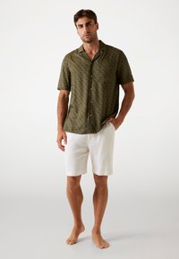 Chemise à manches courtes verte olive avec un motif subtil, dotée d'un col et de boutons, associée à un short en lin blanc.