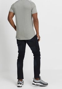 Ljusgrå kortärmad skjorta med rundad nederkant, kombinerad med mörkblå skinnyjeans och gråsvarta sneakers.