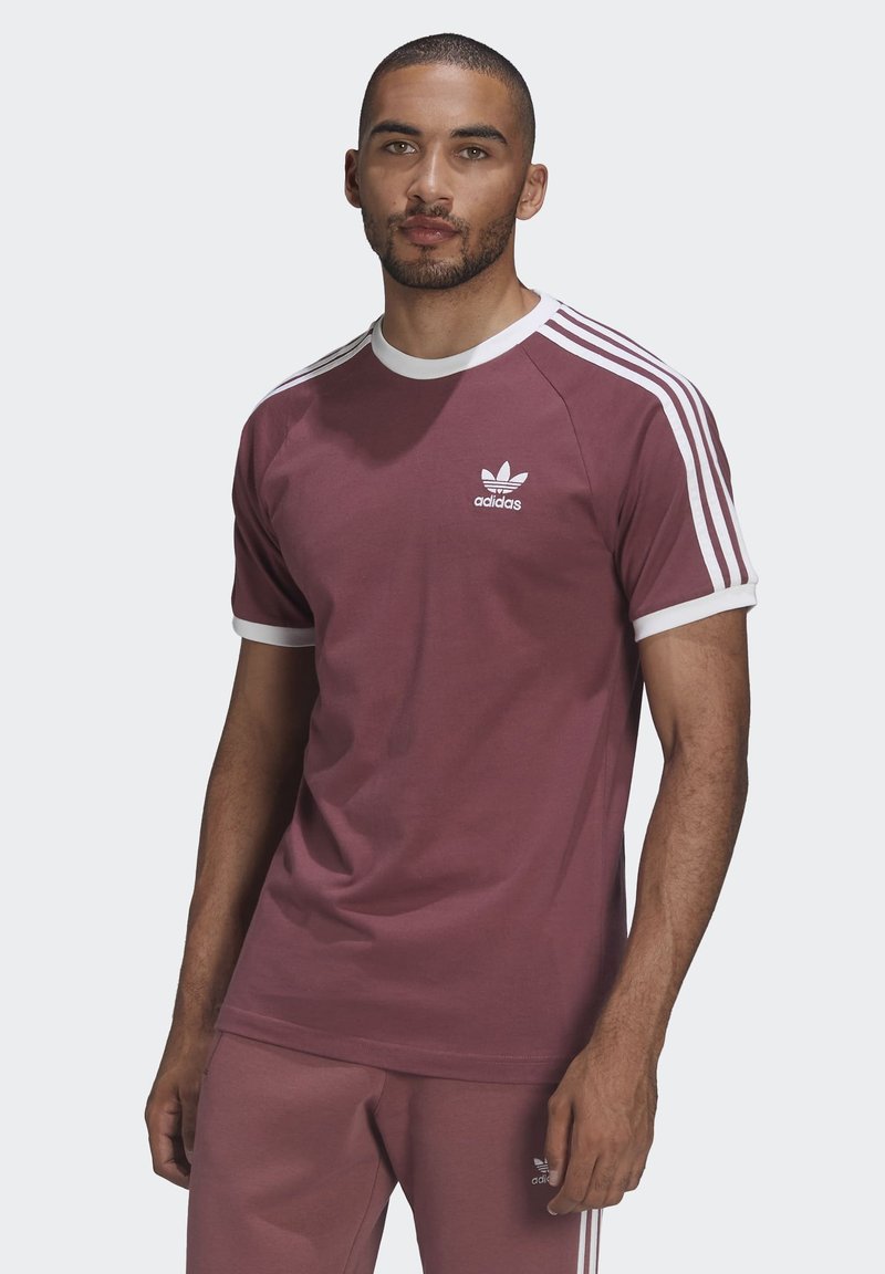 Tumši sarkans kokvilnas T-krekls ar baltām detaļām un trim baltām svītrām uz piedurknēm. Uz krūtīm ir neliels balts Adidas logo.