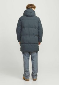 Dark gray puffer coat with a large hood, featuring quilted sections for insulation. Worn with light blue loose-fitting jeans and brown shoes.