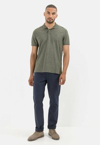 Olijfgroene polo met korte mouwen, gestructureerde stof, met een twee-knopen sluiting, gecombineerd met marineblauwe broeken en beige suède schoenen.
