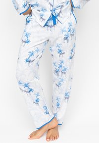 Witte pyjama set met een blauw zebrapatroon en palmbomen, met blauwe bies op de broek en het shirt, met een gladde stofstructuur en een relaxte pasvorm.