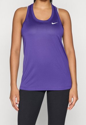 Frau trägt ein ärmelloses lila Nike-Tanktop und schwarze Leggings, steht vor einem schlichten hellen Hintergrund.