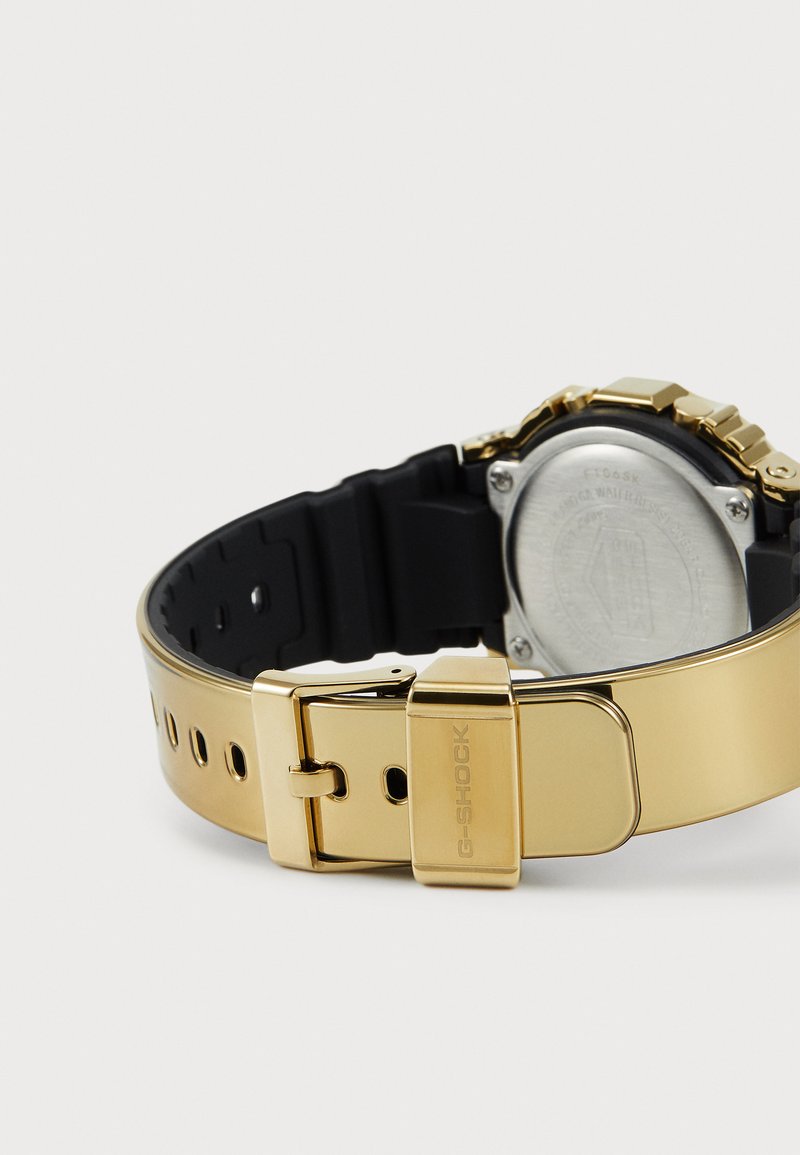 Orologio G-Shock color oro con cinturino in gomma nera. Presenta accenti metallici, chiusura a scatto e retro in acciaio inossidabile.
