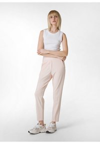 Witte geribbelde mouwloze top, lichtroze op maat gemaakte broek met zakken, en chunky witte sneakers met grijze en groene accenten.