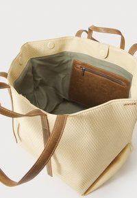 Beige geflochtene Tragetasche mit braunen Ledergriffen, ausgestattet mit einem grünen Stoffinneren und einem braunen Reißverschlussfach im Inneren.