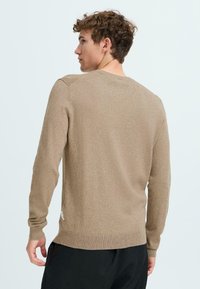 Maglione beige realizzato in morbido materiale a maglia, con scollatura rotonda, maniche lunghe, orlo a coste e una finitura leggermente testurizzata.