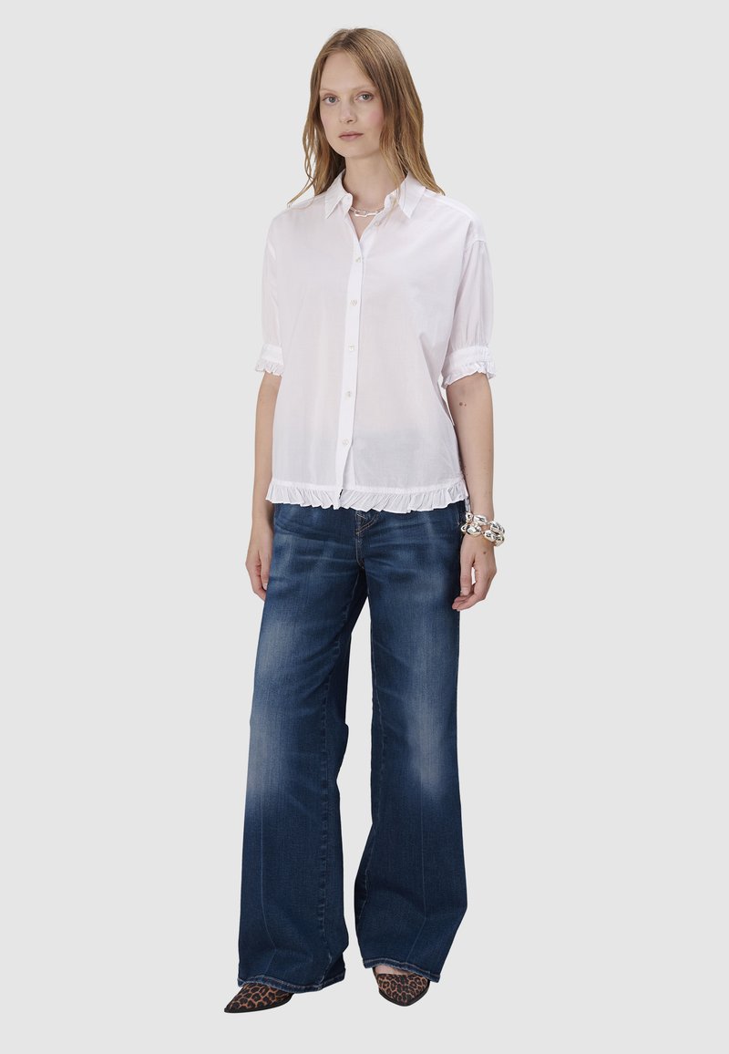 Chemise blanche à manches courtes avec un ourlet volanté, associée à un jean foncé évasé. Les chaussures sont à motif léopard.