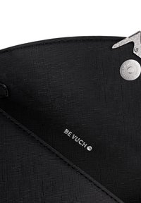 Close-up of black textured bag interior with silver magnetic clasp and small metal "BE VUCH" logo.