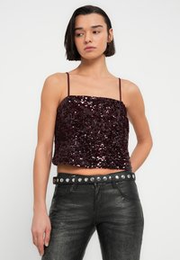 Top court bordeaux à sequins avec fines bretelles, présentant un col carré et une coupe ample, assorti d'une ceinture noire cloutée et d'un pantalon texturé.