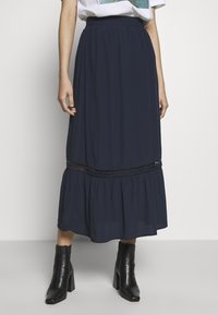 Mörkblå maxikjol i lätt tyg, med ett flerskiktat mönster och spetsdetalj, samt elastisk midja. Kombinerad med svarta ankelstövlar.