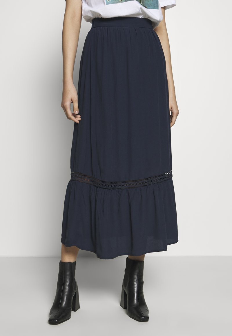 Mörkblå maxikjol i lätt tyg, med ett flerskiktat mönster och spetsdetalj, samt elastisk midja. Kombinerad med svarta ankelstövlar.