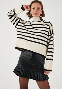 Gestreepte coltrui in crème en zwart, met ribbelstructuur. Gecombineerd met een zwarte, geplooide faux leren rok, wat zorgt voor een gelaagd uiterlijk.