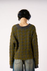 Vihreä ja harmaa kuvioitu ylipitkä neule, jossa on teksturoitu, pörröinen materiaali ja ribattu kaula-aukko, päällä vaaleansiniset raidalliset farkut.