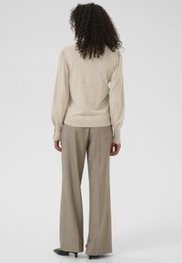 Pull beige à manches longues avec épaules bouffantes, associé à un pantalon large marron clair. Le pull présente des poignets boutonnés pour plus de détail.