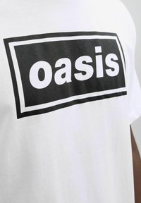 Balta medvilnės marškinėliai su dideliu juodu stačiakampiu grafiku, kuriame užrašyta žodis "oasis" bold baltu tekstu. Paprastas, kasdieniškas dizainas.