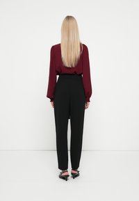 Blusa burgundy de mangas longas com mangas bufantes, combinada com calças pretas de cintura alta, apresentando um corte reto e um ajuste elegante, vista de costas.