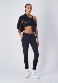 Top corto atlético negro con el logo "CHAMP", joggers negros a juego con bolsillos y zapatillas blancas. Tela suave, diseño ajustado.